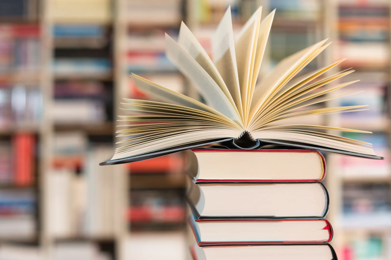 Aufgeschlagenes Buch auf einem Bücherstapel vor Bücherregalen